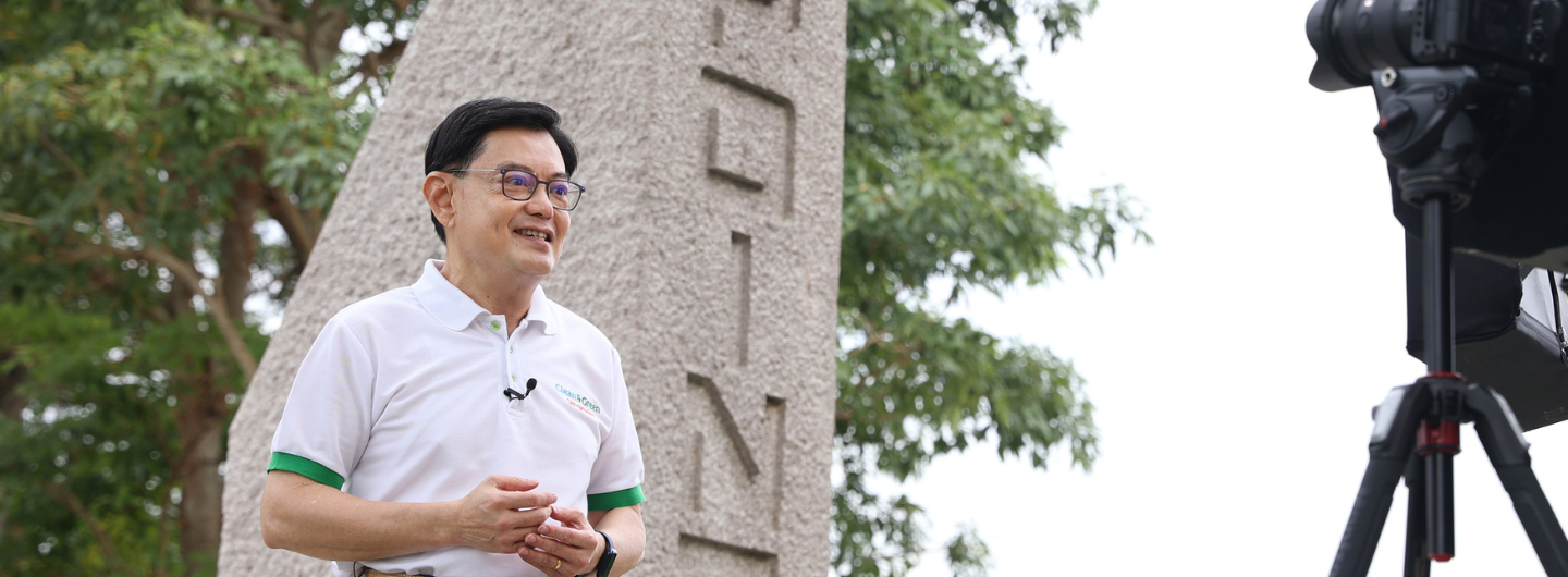 Man in white polo (Clean & Green logo) near a stone obelisk and a camera on a tripod.